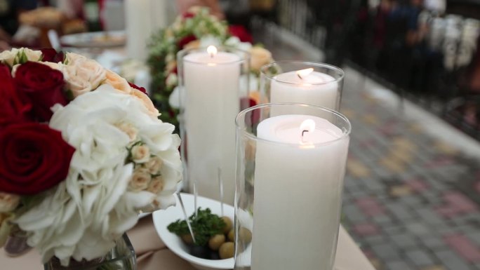 优雅的婚宴表与白色蜡烛在透明的花瓶，充满活力的红色和白色的花卉安排的客人座位在庆祝活动。模糊的背景与
