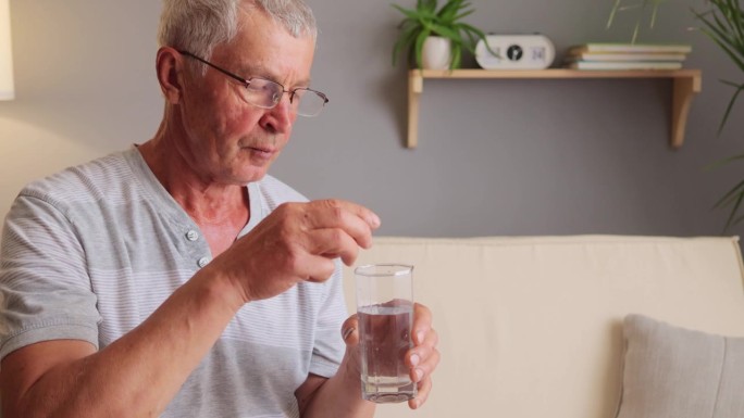 患有高血压或抑郁症的老人坐在客厅的沙发上用药，把药滴到杯子里喝。