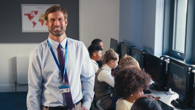 在信息技术课上，微笑的男中学老师和学生在电脑前的合影