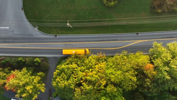 黄色校车行驶在美国郊区的街道上。秋季航拍自上而下跟踪拍摄。