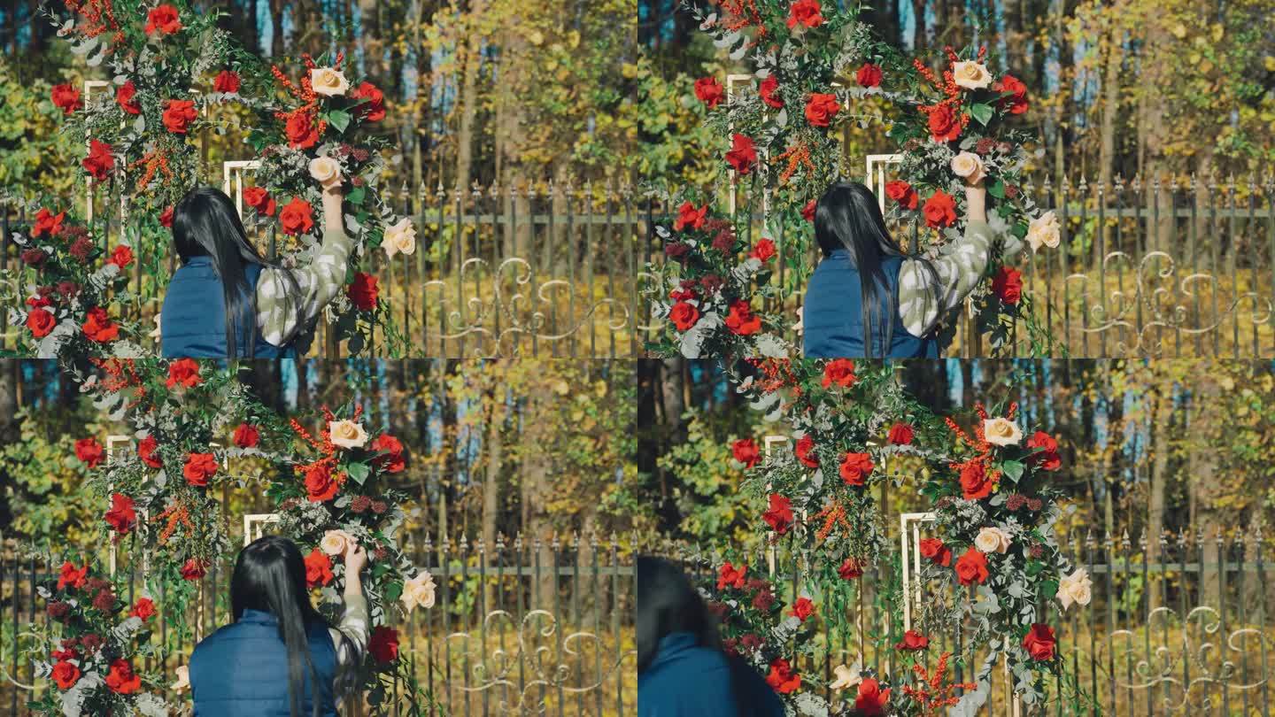 一位妇女将一枝黄玫瑰系在插花上。花店装饰设计师用鲜花制作婚礼拱门