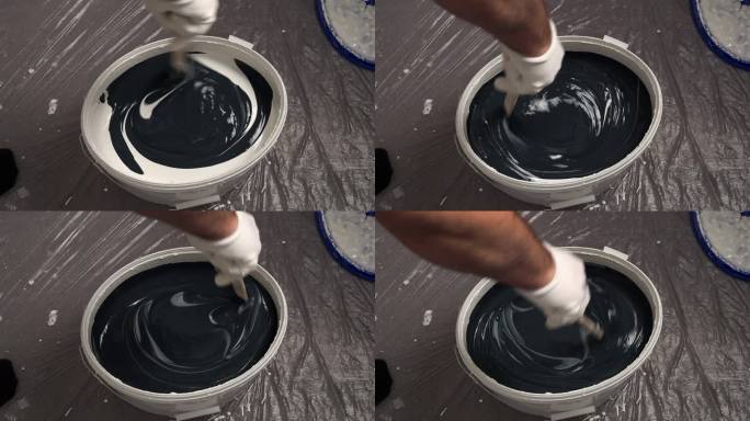 一个工人在桶里混合颜料来粉刷墙壁。