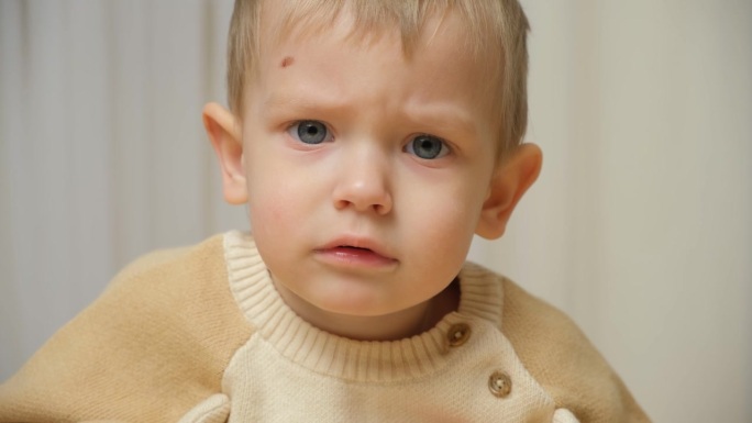 一个严肃的两岁孩子的肖像，蓝眼睛，皱着眉头，看着镜头说话。