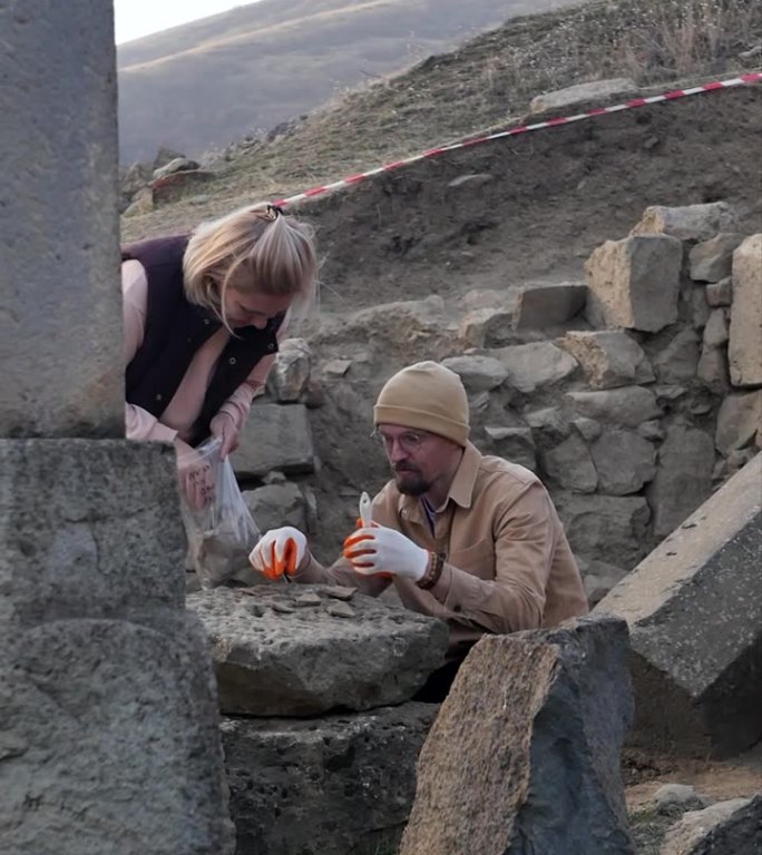 竖屏考古发掘。年轻的考古学家，一男一女，正在一座被毁城市的古建筑废墟中探索文物。历史发现和细节