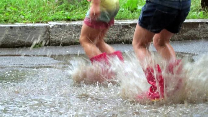 特写镜头。一个穿着粉色胶靴的小女孩在雨坑里快乐地跳着。缓慢的运动。4 k的视频。