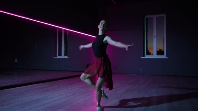 住相机。一个美丽的芭蕾舞演员在霓虹灯照亮的黑暗舞蹈大厅里优雅的动作。