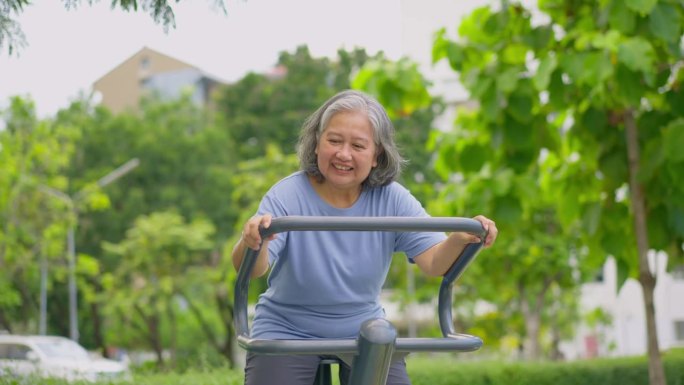 在公园健身站随意锻炼的亚洲老年妇女。代表以运动永葆青春，露天健身，身体健康的理念。城市公园户外健身器