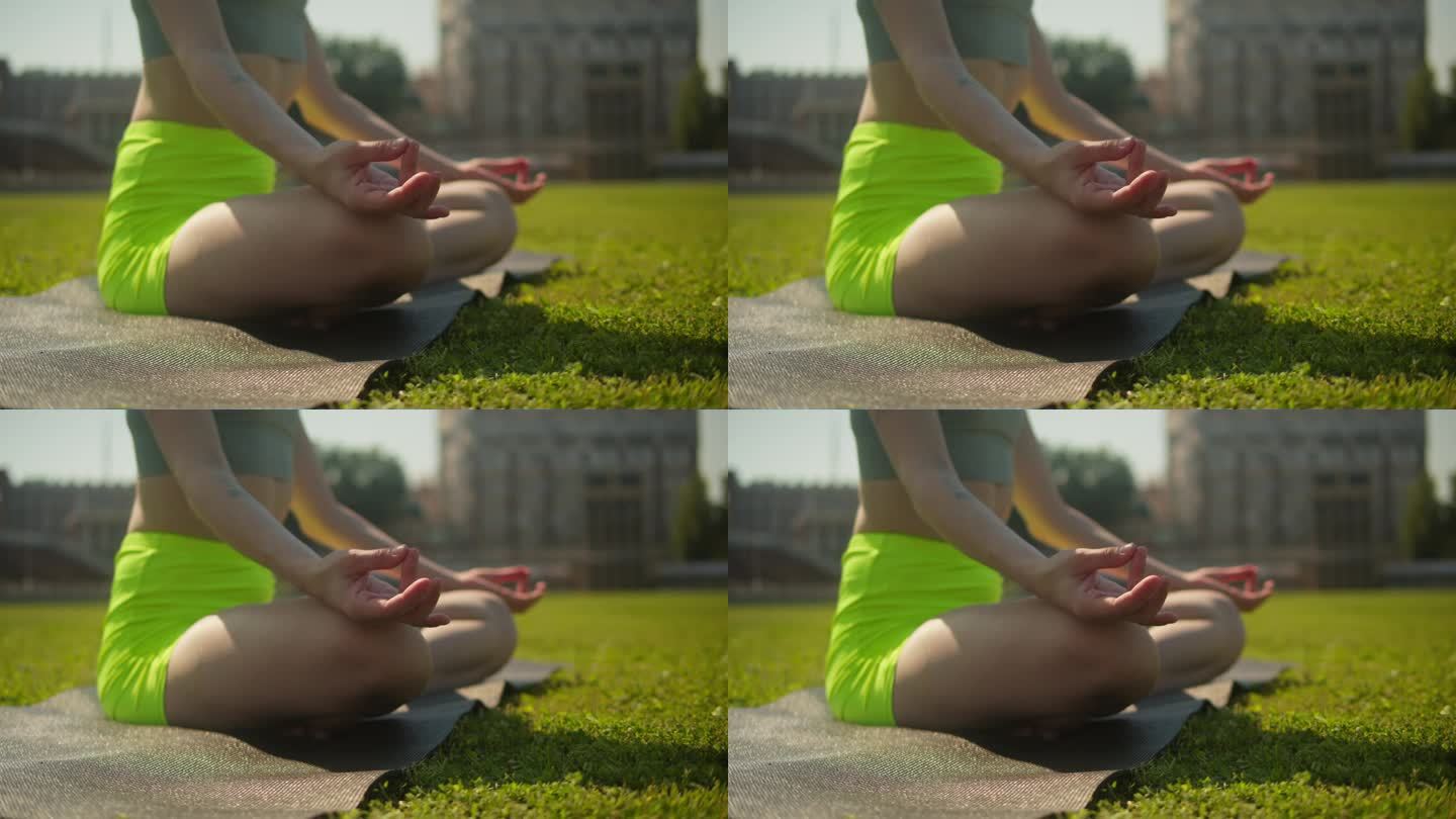 年轻女子在体育场的绿草地上沉思。拍摄女性在户外做瑜伽练习，平静的冥想，自然