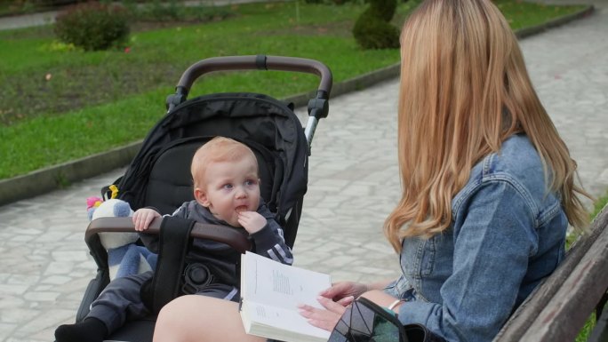 妈妈在看书，宝宝在公园里玩婴儿车