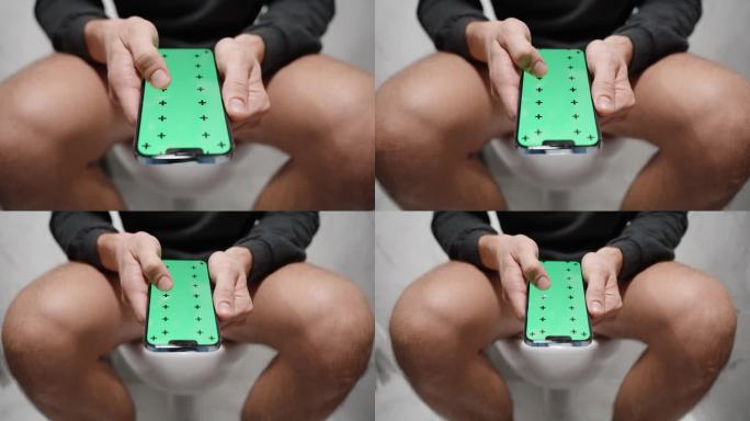 一名男子坐在马桶上，滚动绿色屏幕查看布局。多莉。在浴室长时间使用智能手机的概念。