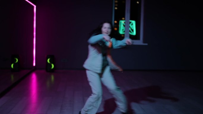 住相机。一个女孩在黑暗的舞蹈大厅里用霓虹灯照亮的镜子跳嘻哈舞。