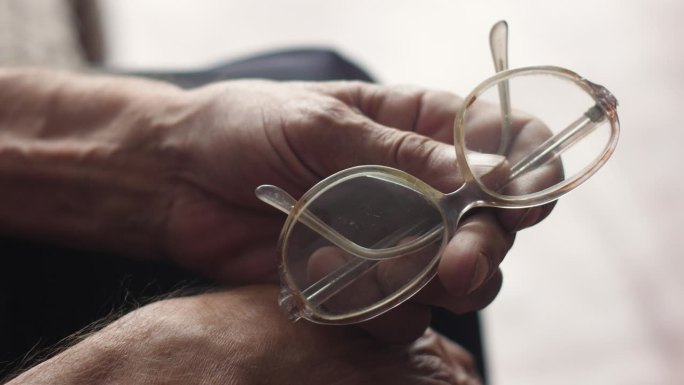拿着眼镜的退休老人的手。老年人戴眼镜的概念。老年视力减退真正的70岁老人