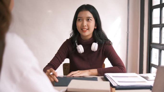 迷人的亚洲大学生使用笔记本电脑和平板电脑与一群朋友一起学习英语课堂，社交媒体和教育理念。