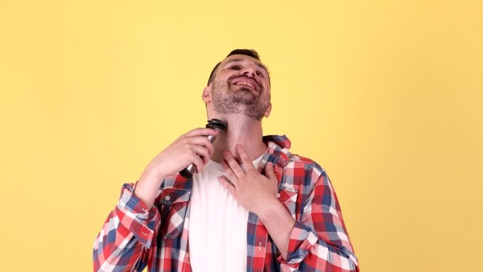 黄色背景下，男子正在用电动修面机刮胡子。