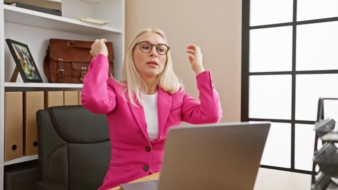 工作过度、压力大的年轻金发女商人在办公室里专心于她的笔记本电脑工作，同时又担心各种问题。