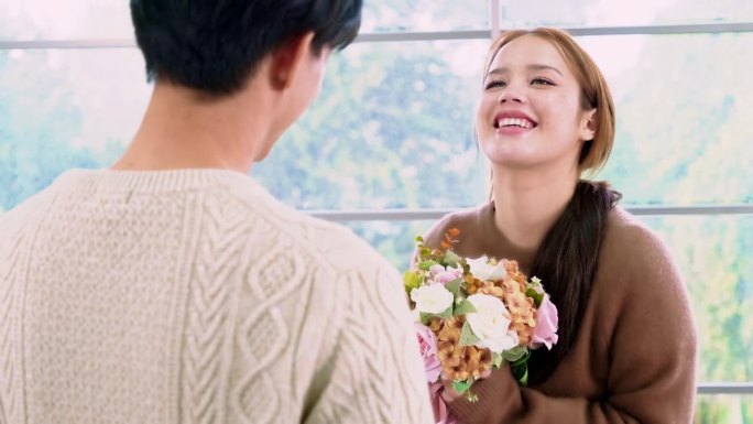 一名年轻的亚洲男子给女友一个惊喜，在她的周年纪念日回家时送给她一束玫瑰和鲜花。亚洲女人喜欢收到男友送