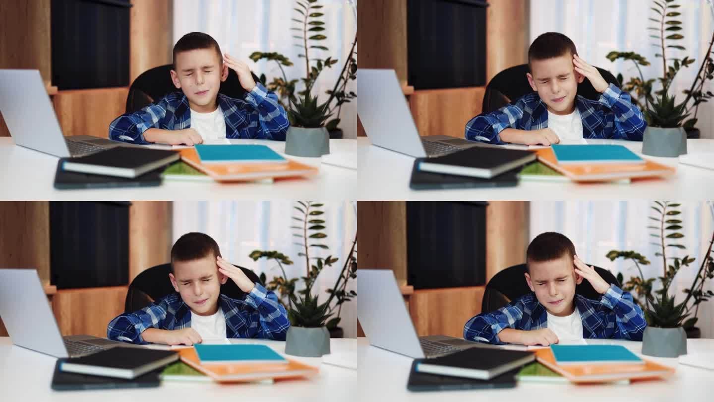 累的小家伙摸着头闭着眼睛，在无线笔记本电脑上上网时头痛不已。身体不适的白种小孩，穿着便装，需要照顾和