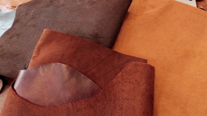 三种不同的棕色和焦糖色的皮革躺在工作台上，准备由一个小工匠企业加工成皮革制品