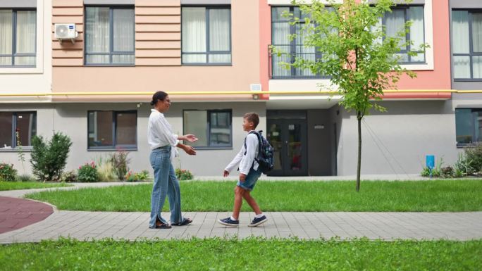 一位非裔美国母亲站在学校大楼外，在一天的学习结束后，温暖地拥抱着她的儿子。在学校度过了漫长的一天后，