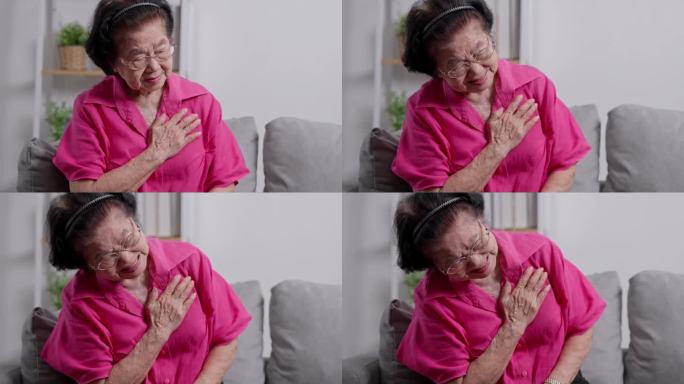 一位患有心脏病的亚洲老年祖母坐在客厅的沙发上捂着胸口。医疗急救和医疗保险保障理念