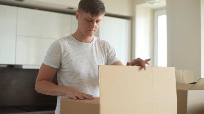 专注的年轻人用胶带把纸板箱包好，准备搬进新居。男性用胶辊包装家具和家庭物品