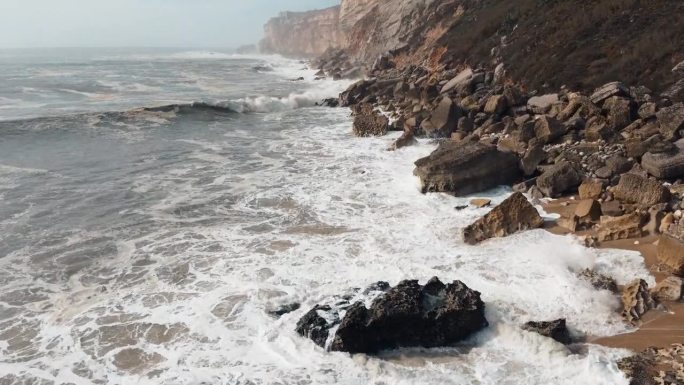 航拍镜头捕捉到海浪冲击葡萄牙纳扎雷崎岖海岸的不屈不挠的力量。海洋的不可驯服的力量展现出来。4 k。