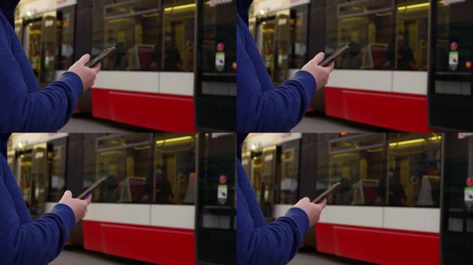 男子在等电车，全神贯注地玩智能手机。场景描绘了城市生活，重点是智能手机的使用。一名男子在电车站刷智能