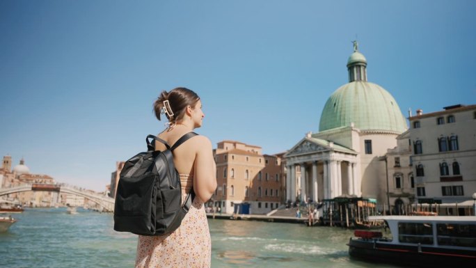 蓝天下度假，年轻女子背着双肩包走向威尼斯运河