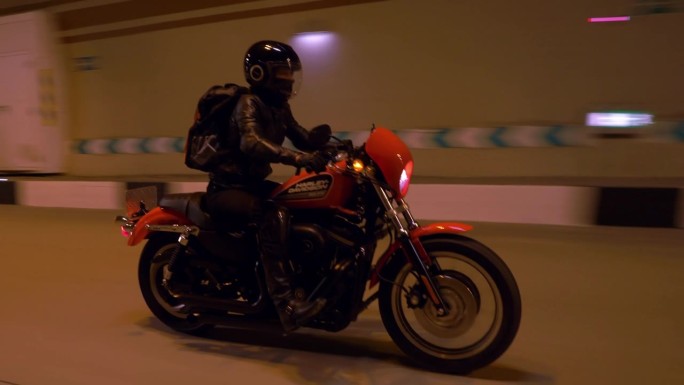 穿着皮夹克的机车女孩骑着摩托车驶入隧道道路。