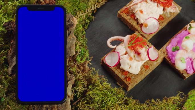 斯堪的纳维亚餐厅订桌应用，送餐手机应用配色度键绿屏，餐点咸味干熏鱼木桌上准备外卖。