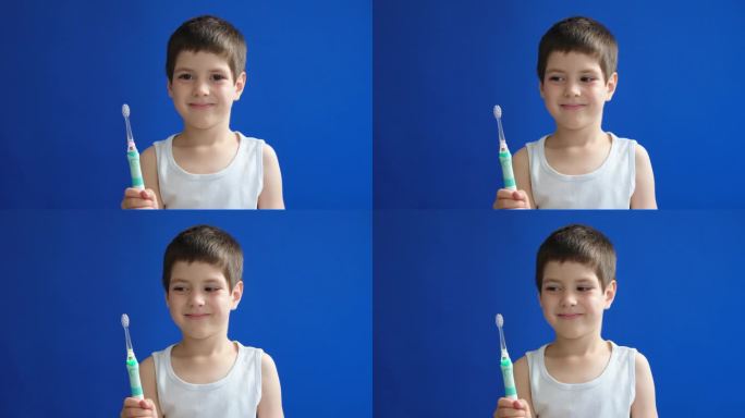 一个六岁的小男孩微笑着拿着一把电动超声波牙刷在蓝色色度键屏幕上。