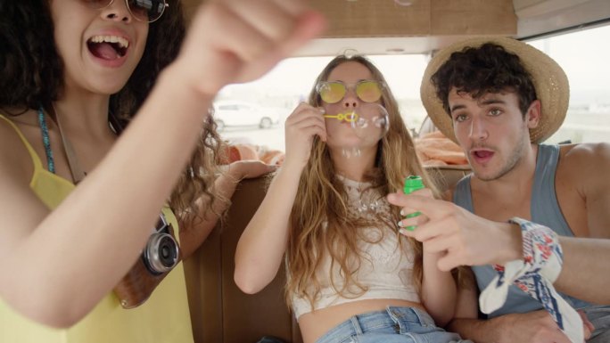 美丽的青少年潮朋友吹肥皂泡在节日在露营车在公路旅行冒险