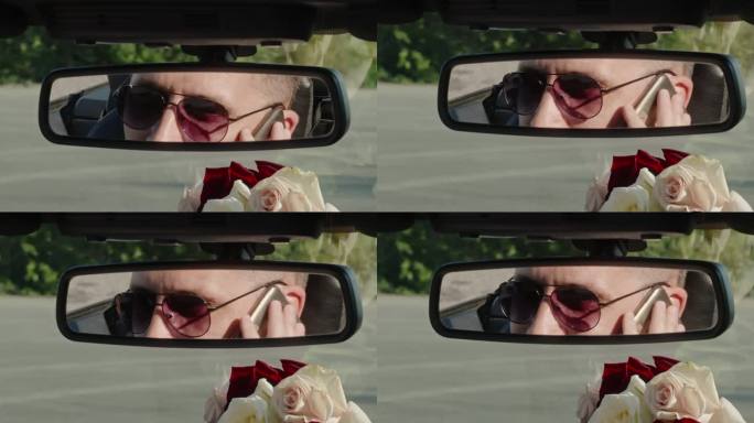 戴墨镜的男子一边抽烟一边在车里说话，镜子上的倒影