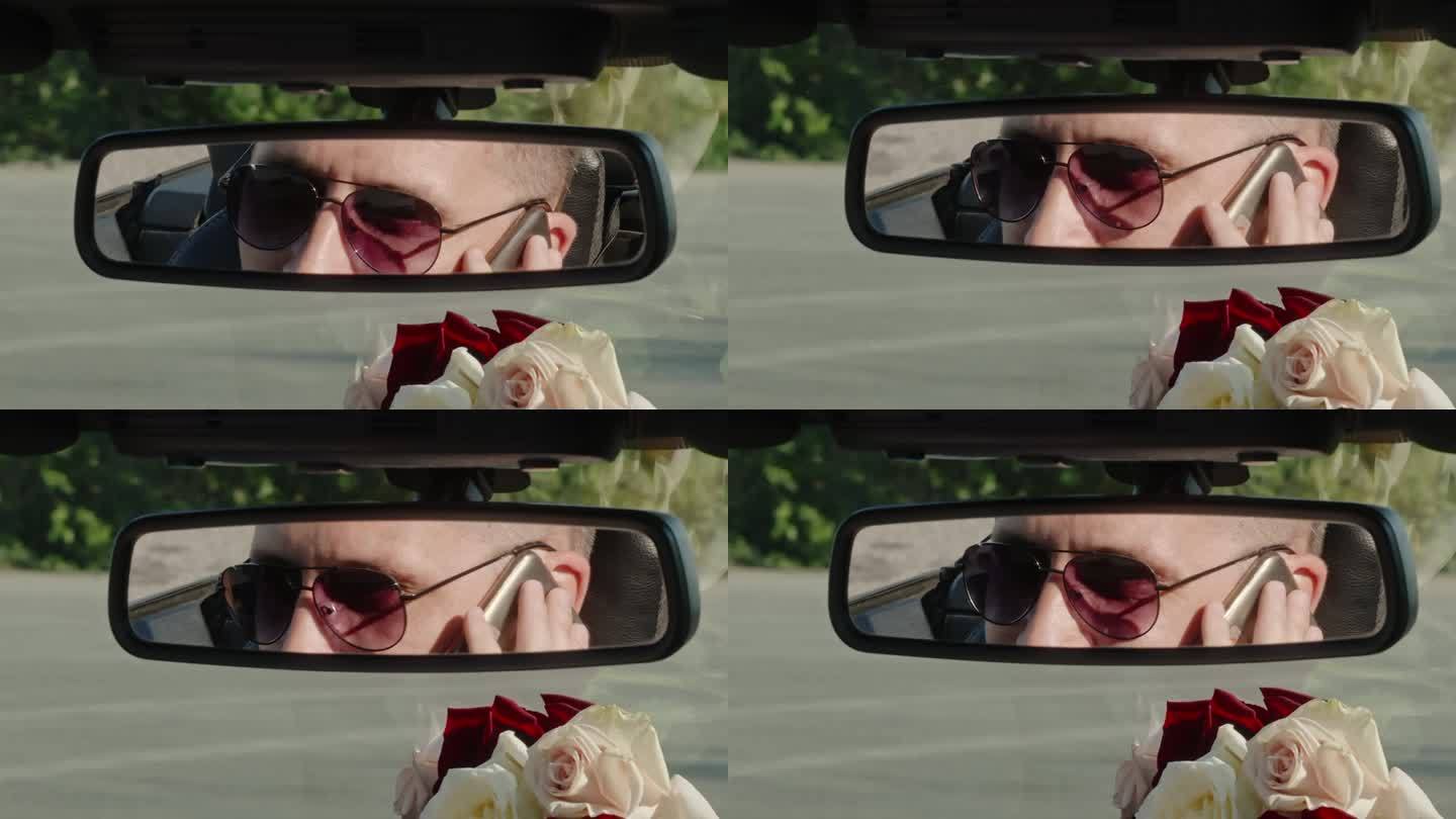戴墨镜的男子一边抽烟一边在车里说话，镜子上的倒影