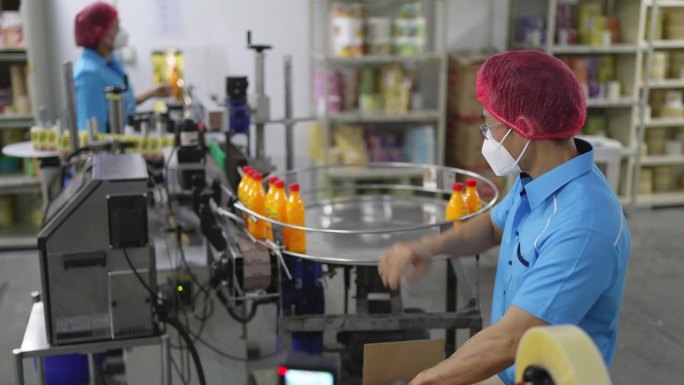 亚洲华人生产线工人在包装前拿起并检查橙汁瓶