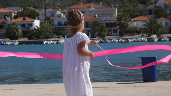 一个小女孩在希腊爱琴海的一个混凝土码头上玩着粉色的体操带