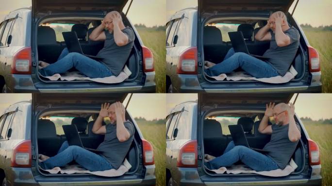 一名穿着休闲装的男子在旅行时，坐在汽车后备箱里的笔记本电脑上抓着自己的头，在商业项目中犯了不可挽回的