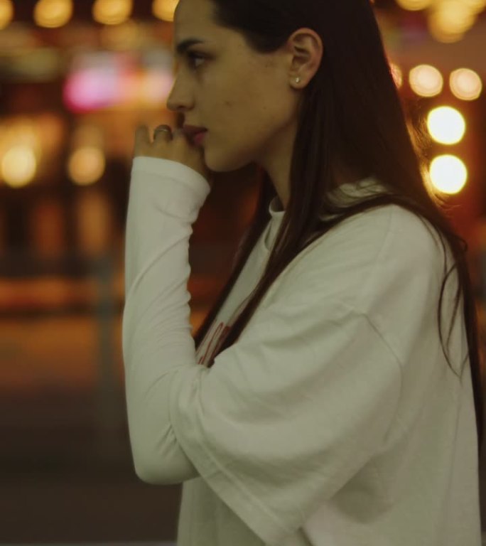 身穿白衣的女孩在夜晚的城市背景下整理着她的头发