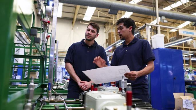 一位男同事在一家水泵厂培训一位新员工，一边拿着机器的蓝图，一边向他解释整个过程