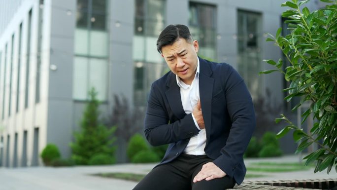一名身着正装的亚洲商人心脏病发作，他正坐在办公楼附近街道的长椅上