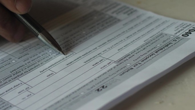 一支笔和一张由一名男子填写的1040税表的特写。税收减免和福利。美国居民的税收