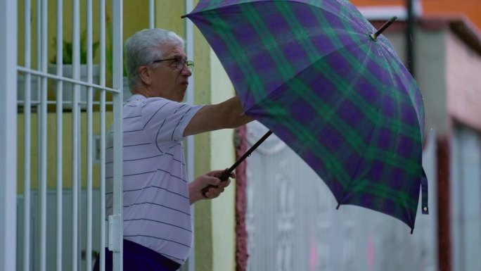 一个成熟的男人在恶劣的天气里撑开雨伞。上了年纪的白种人走在街上，在雨中离开家