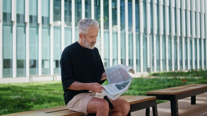 老人在街上看报纸。长得好看的成熟男人休息板凳