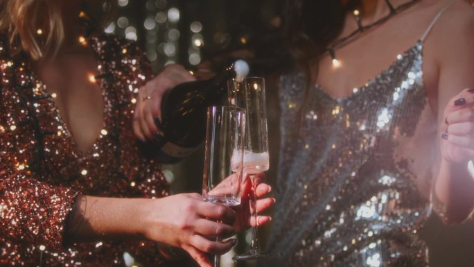 姑娘们把香槟酒倒进圆酒杯里。穿着闪闪发光的裙子的女人，鸡尾酒奶精，小杯