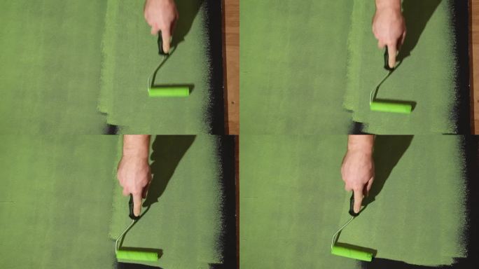 男子用滚筒刷在黑色墙壁上涂绿色颜料，特写。家居装修DIY。手用滚筒刷墙。副本的空间。水性漆。修复。装