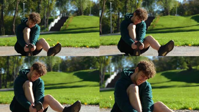 在一个阳光明媚的夏日，一名男子坐在公园里的地上按摩他的脚。这家伙的脸显示出极度的痛苦。真正的时间。户