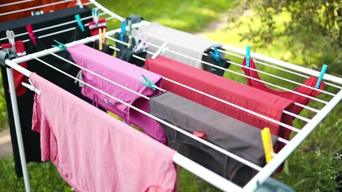 湿女人的衣服挂在干衣机上。洗衣服和做家务。一个女人在室外的晾衣机上挂着不同的衣服，特写