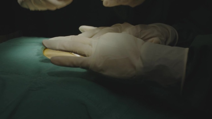 在黑暗的手术室里，医生做完手术后，护士和她的助手正在给病人的伤口消毒，并将消毒的纱布垫和绷带放在病人