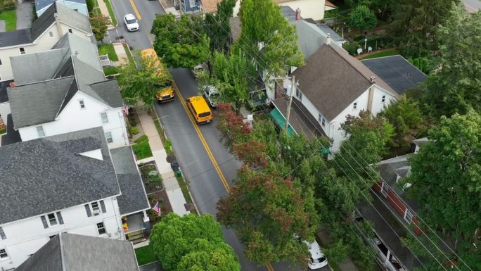 黄色校车行驶在美国城镇街道上。秋日航拍跟踪拍摄。