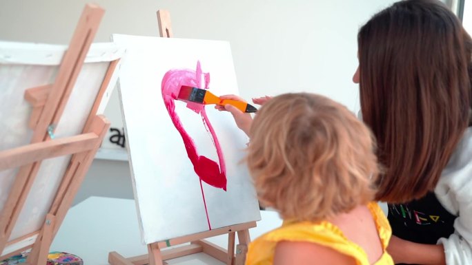 艺术学校的老师在美术课上帮助孩子们画画。妇女教孩子用丙烯酸颜料创作和工作。一群小学生在老师的帮助下学